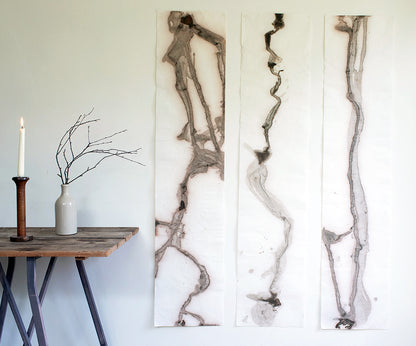 Three river mud spill original artwork paintings on white wall with rustic table to the left. Artwork by Agnes Becker from We Are Stardust